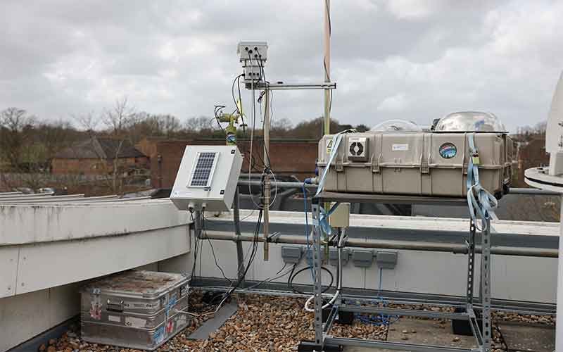 The box with the dome is a sun-tracking Fourier transform infrared spectrometer (FTIR) that measures the greenhouse gases carbon dioxide, methane and carbon monoxide in a column of the atmosphere. Mounted on the pole behind is a Multi-Axis Differential Optical Absorption Spectroscopy (MAX-DOAS) instrument that measures the urban pollutants such as NO2, SO2 and ozone.