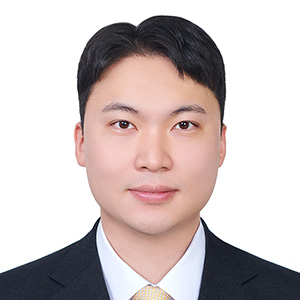 Headshot of a Hyunwoo Shin in a dark suit, white shirt, and light-colored tie against a light gray background.