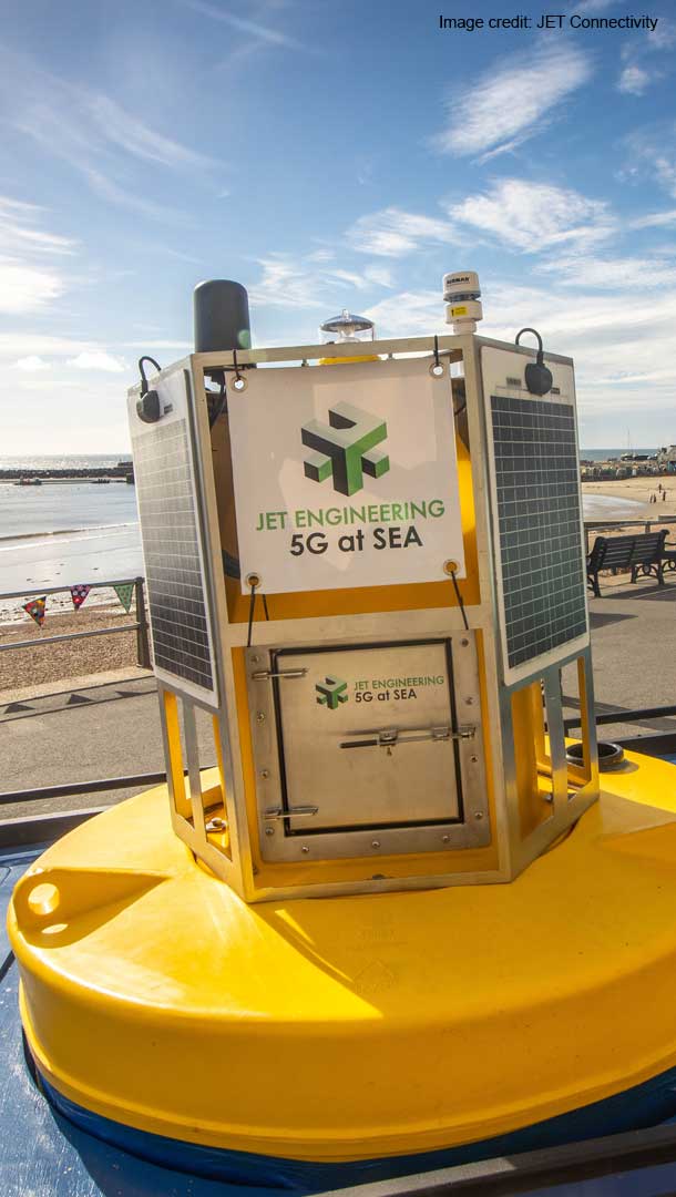 Yellow buoy with panels on side which look like solar panels on the back of a vehicle with the sea on a sunny day in the background